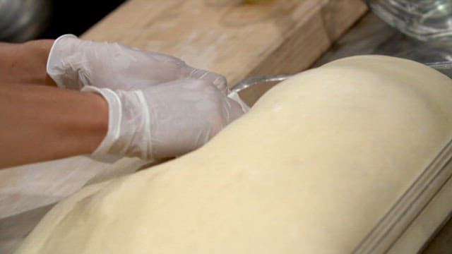 Taking a large piece of dough and placing it on a wooden cutting board