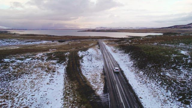 Car traveling on a snowy road by a lake