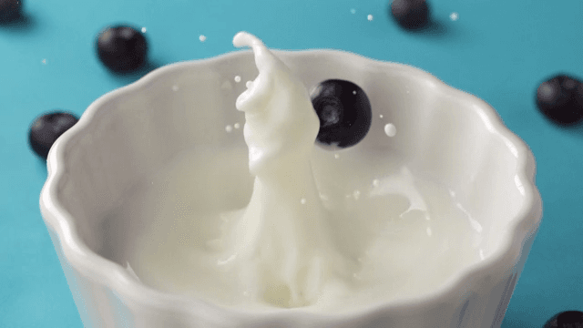 Blueberry falling into a bowl of milk