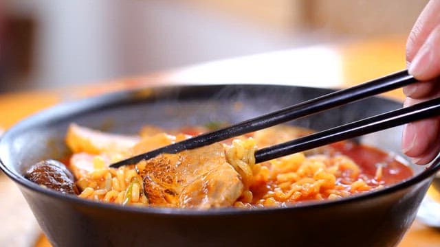 Chopsticks holding ramen with pork slice