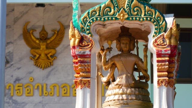 Decorative statue in front of a building with buddhist symbolic carvings.