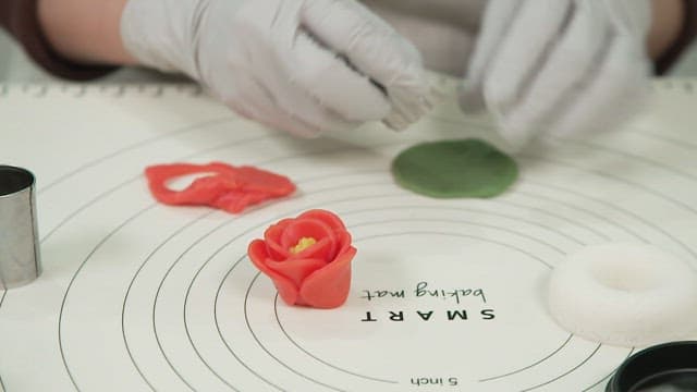 Gloved hands shaping icing into decorative flowers on a baking mat