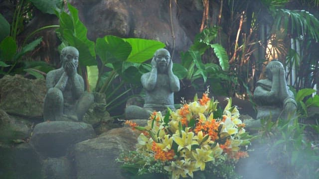 Three wise monkey statues with flowers in a garden in a temple