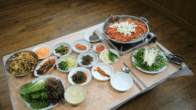 Table full of spicy duck bulgogi, ssam vegetables, and various Korean side dishes
