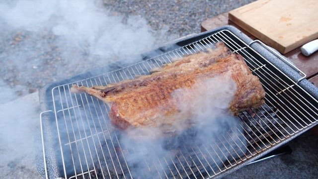 Large piece of meat smoking on the grill outdoors.