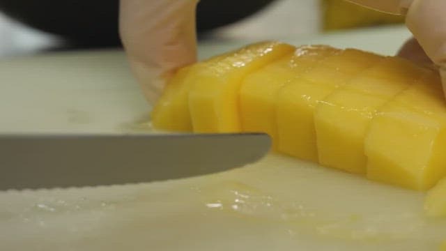 Hands slicing ripe yellow mango on white cutting board.