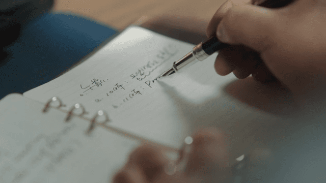 Person Writing in Notebook at Desk