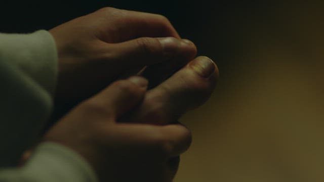 Person examining their injured toenail in dim lighting