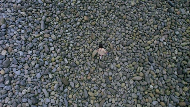 Person Walking on Pebble Beach with Shoes in Hand
