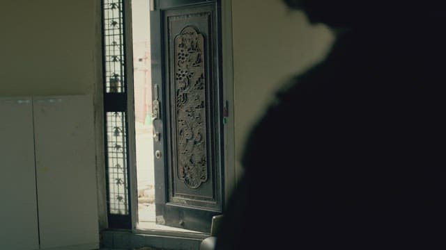 Woman closing the front door of her home and sits down on the sofa.