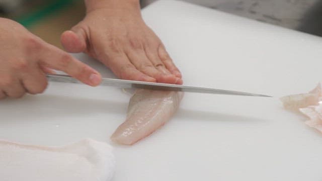 Cutting raw fish with a knife on a kitchen cutting board