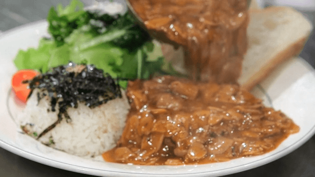 Pouring sauce over hamburger steak plated with rice and bread