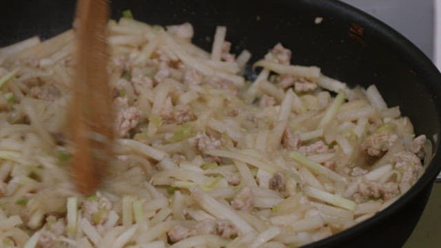 Stir-frying white radish and meat in a black frying pan