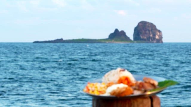Plate of assorted food on a wooden post near the ocean with an island in the background.