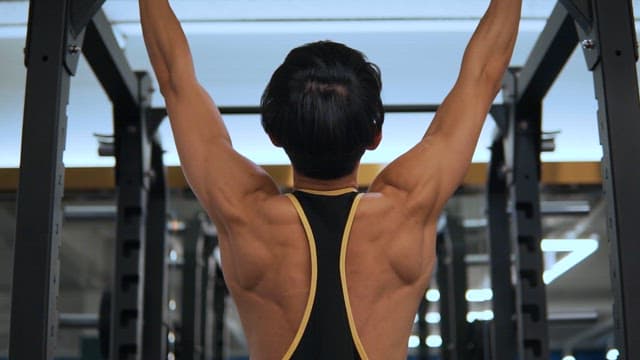 Muscular back view of a man doing pull-ups at the fitness center
