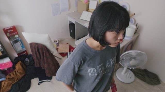 Woman staring at something in a messy room with books and clothes