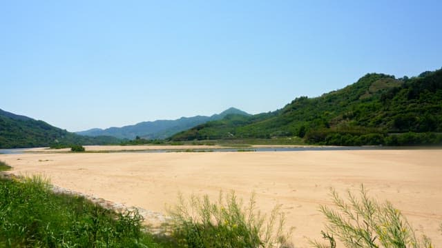 Wide sandy riverbed surrounded by green mountains under clear sky