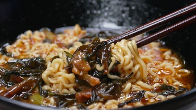 Chopsticks lifting ramen noodles in a bowl