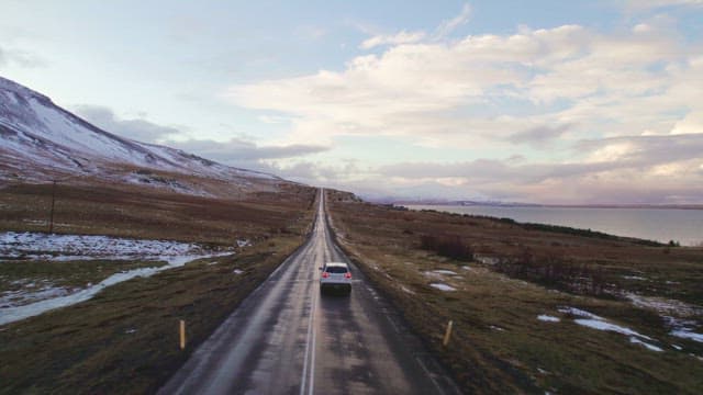Car driving on the road next to a snowy mountain