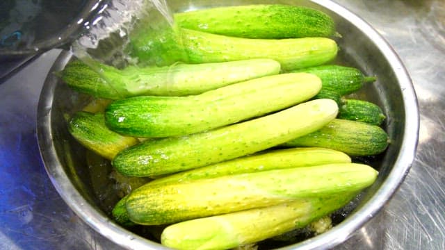 Cucumbers being washed in a metal bowl