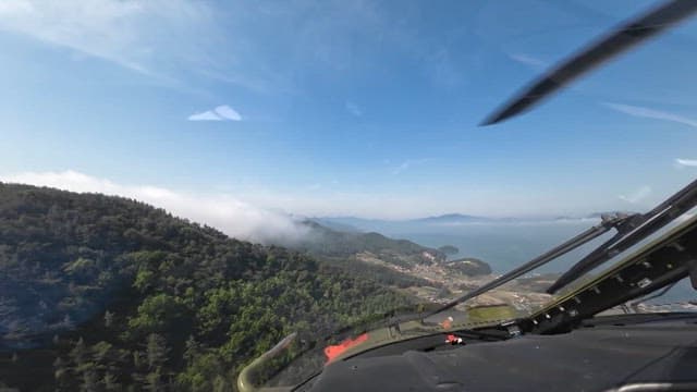 Forested mountains and coastal landscape from a helicopter cockpit on a clear day
