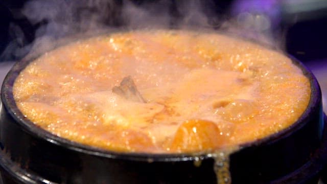 Duck soup overflowing from an earthen pot on a gas stove