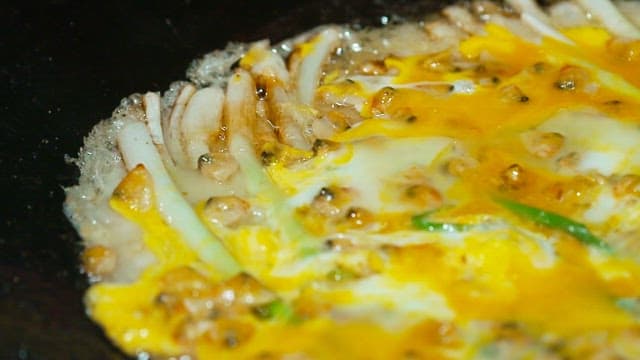 Egg and seafood and green onion pancake cooking in a pan