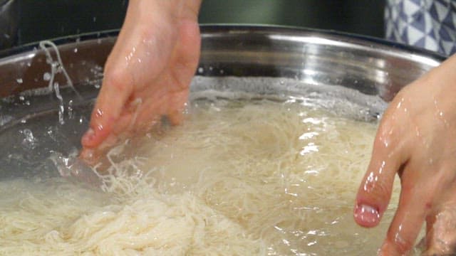 Hands washing noodles in a large bowl