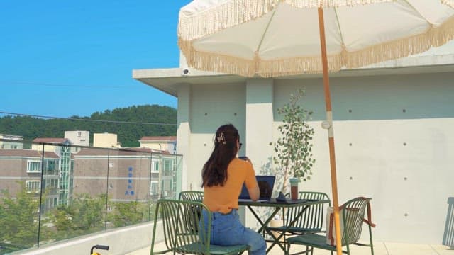 Woman Using Laptop at Rooftop Table with Umbrella