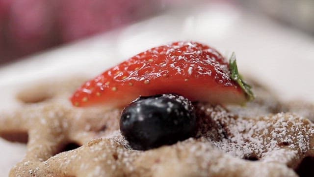 Powdered sugar sprinkled on waffles topped with strawberry and blueberry