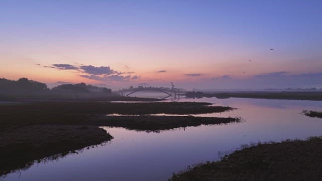 Calm river at sunset with a bridge
