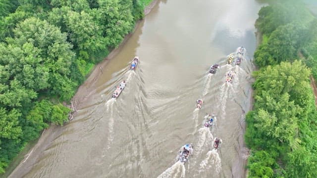 Boats cruising down a river among lush forests on a clear day