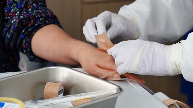 Healthcare worker applies a bandage to a patient's hand with ringer's solution inserted