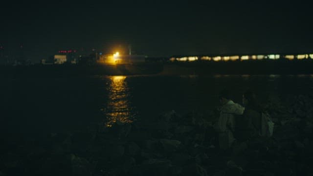 Two students sitting side by side on a beach with lights shining on them