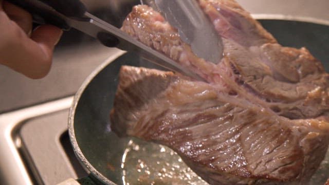 Beef steak being cooked in a frying pan