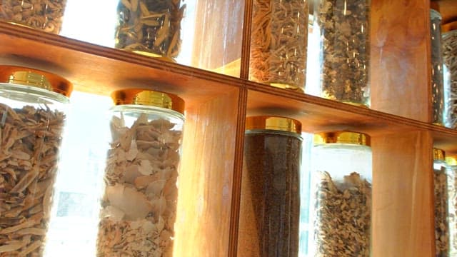 Rows of jars filled with various dried herbs on a wooden shelf