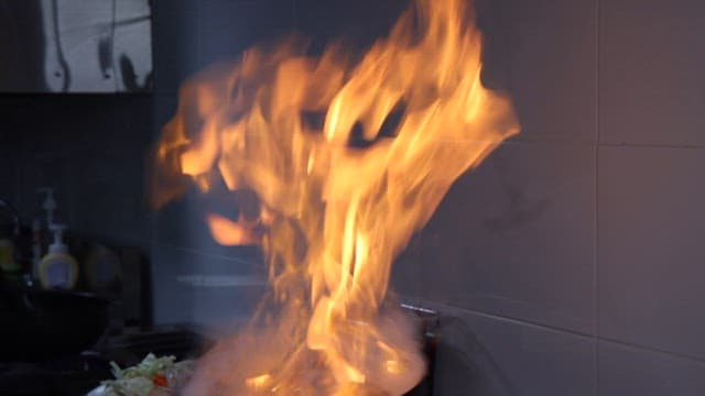 Chef preparing a flaming stir-fried squid on a gas stove in a kitchen