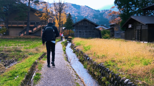 Man Walking Down a Scenic Village Path in Autumn