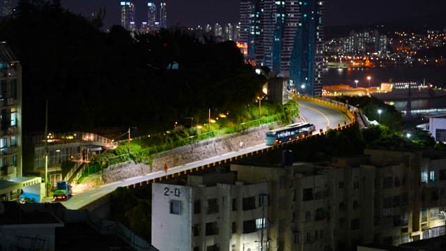 Buses and cars passing on a hill road near a residential area in the city