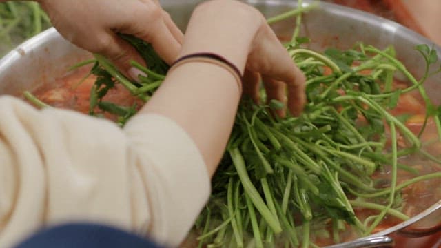 Fresh water parsley going into a boiling hot pot in a pot