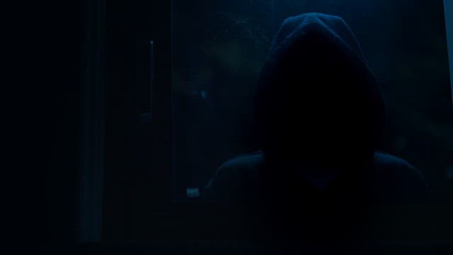 Hooded figure standing outside in the dark at night