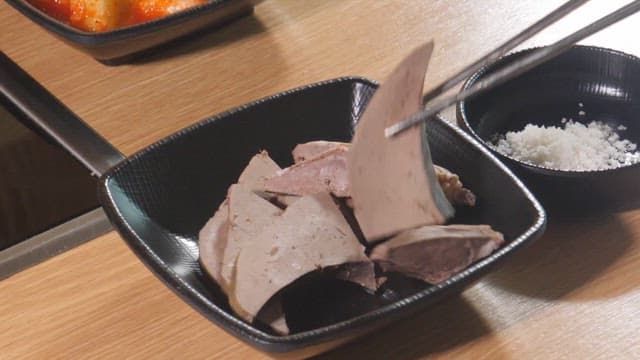 Slices of liver being dipped into salt
