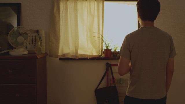 Man smoking at home looking out a sunny window
