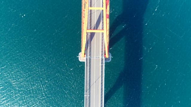 Aerial view of a red bridge crossing the blue ocean on a sunny day