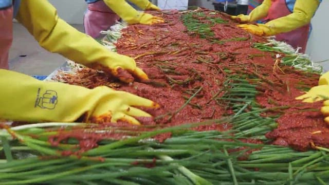 Workers preparing green onion kimchi in a food processing facility