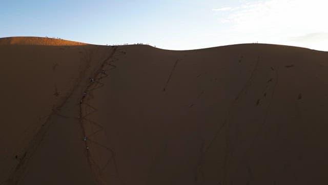 People climbing a large sand dune at sunset