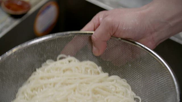 Hand holding a strainer with cooked noodles