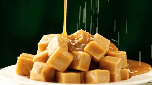 Pouring caramel sauce over caramels piled on a white plate
