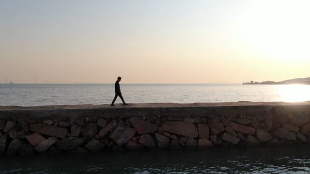 Person walking on a breakwater with the peaceful sea at dusk