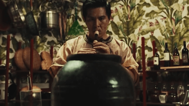 Man playing a flute in front of a brown jar